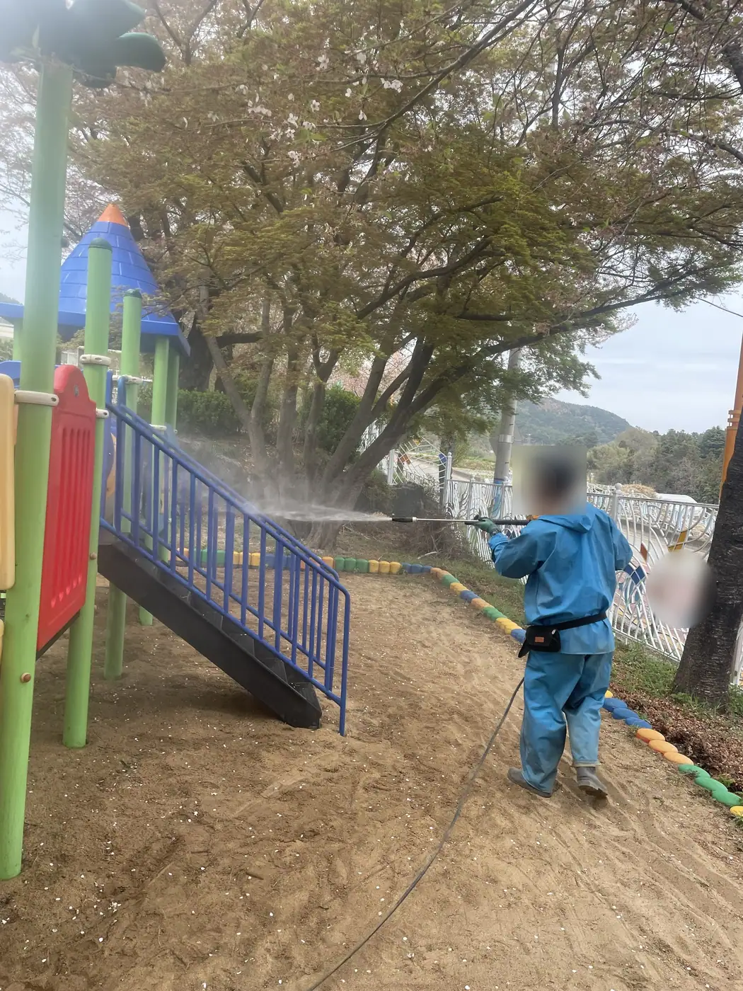 부산 기장군의 한 유치원 놀이터에서 방수복과 헬멧을 갖춘 작업자가 고압 세척건으로 놀이대 계단을 세척하는 모습