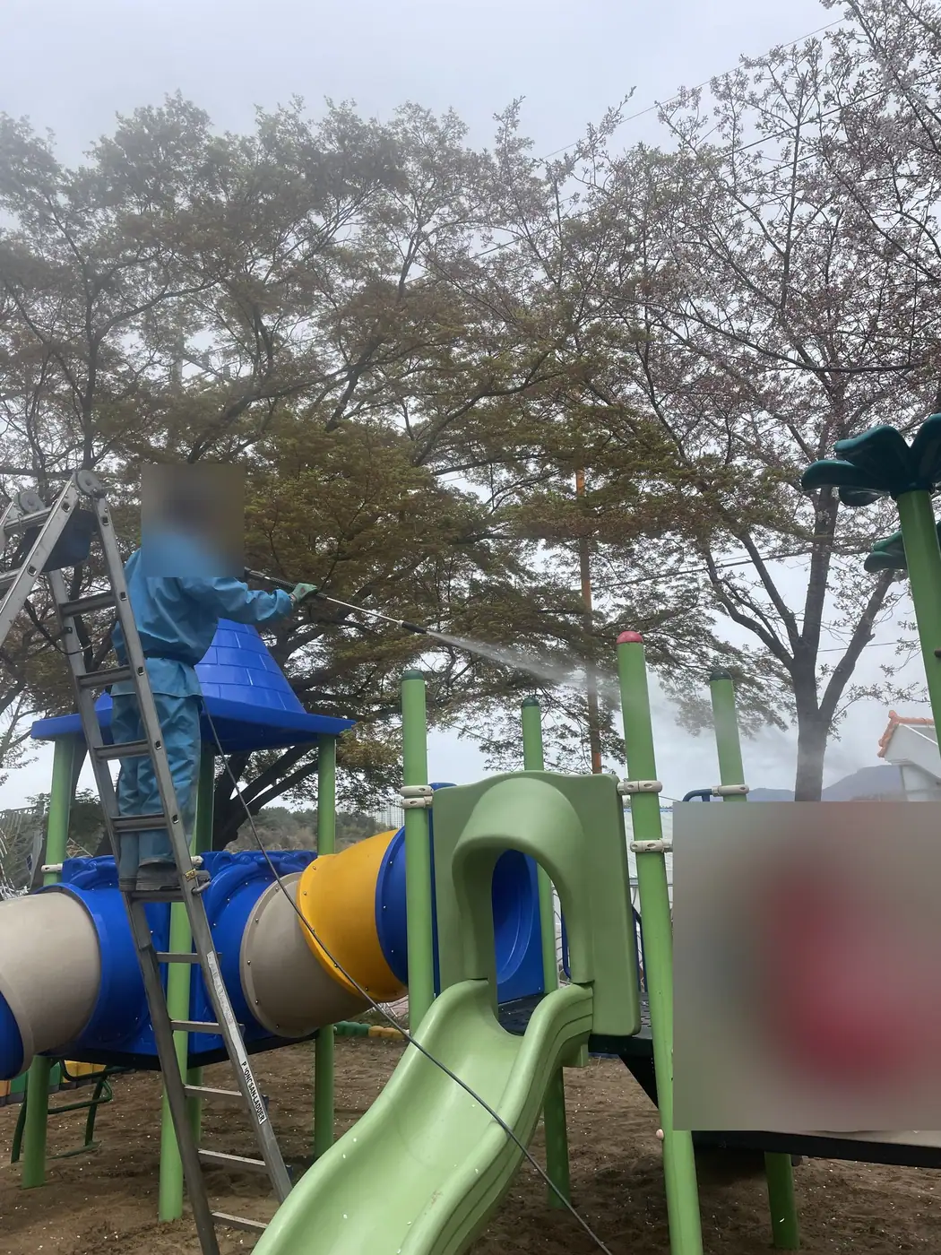 접이식 사다리에 올라선 작업자가 놀이대 지붕 높이에서 고압수를 뿌리는 모습