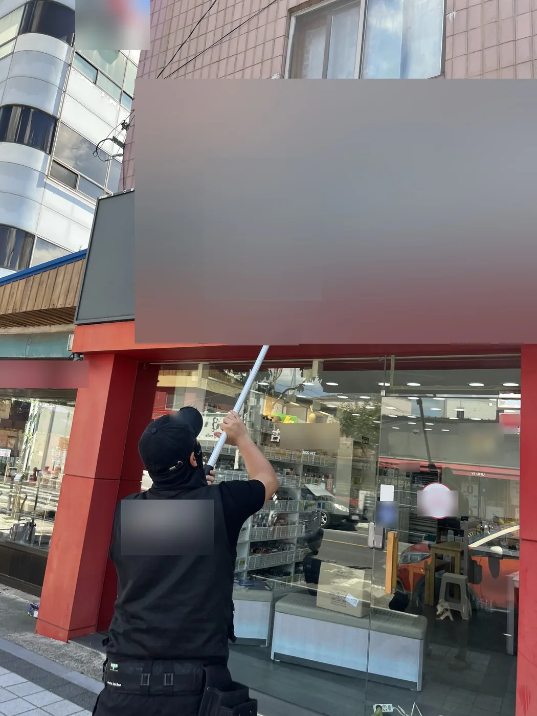 작업자가 세척 폴대를 들어 접힌 어닝 덮개 위 간판면과 입체 글자 둘레를 씻는 장면