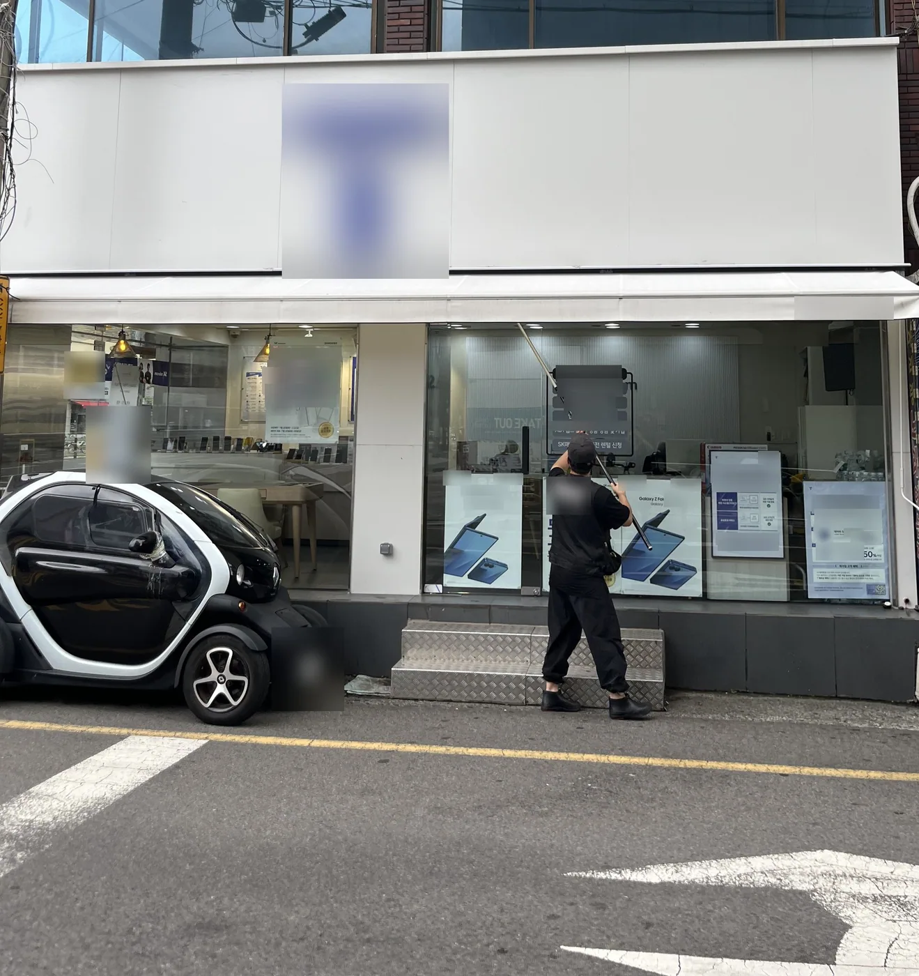 울산 중구 휴대폰 매장 옆면 유리 앞에서 검은 작업복 작업자가 긴 막대를 접힌 어닝에 거는 모습