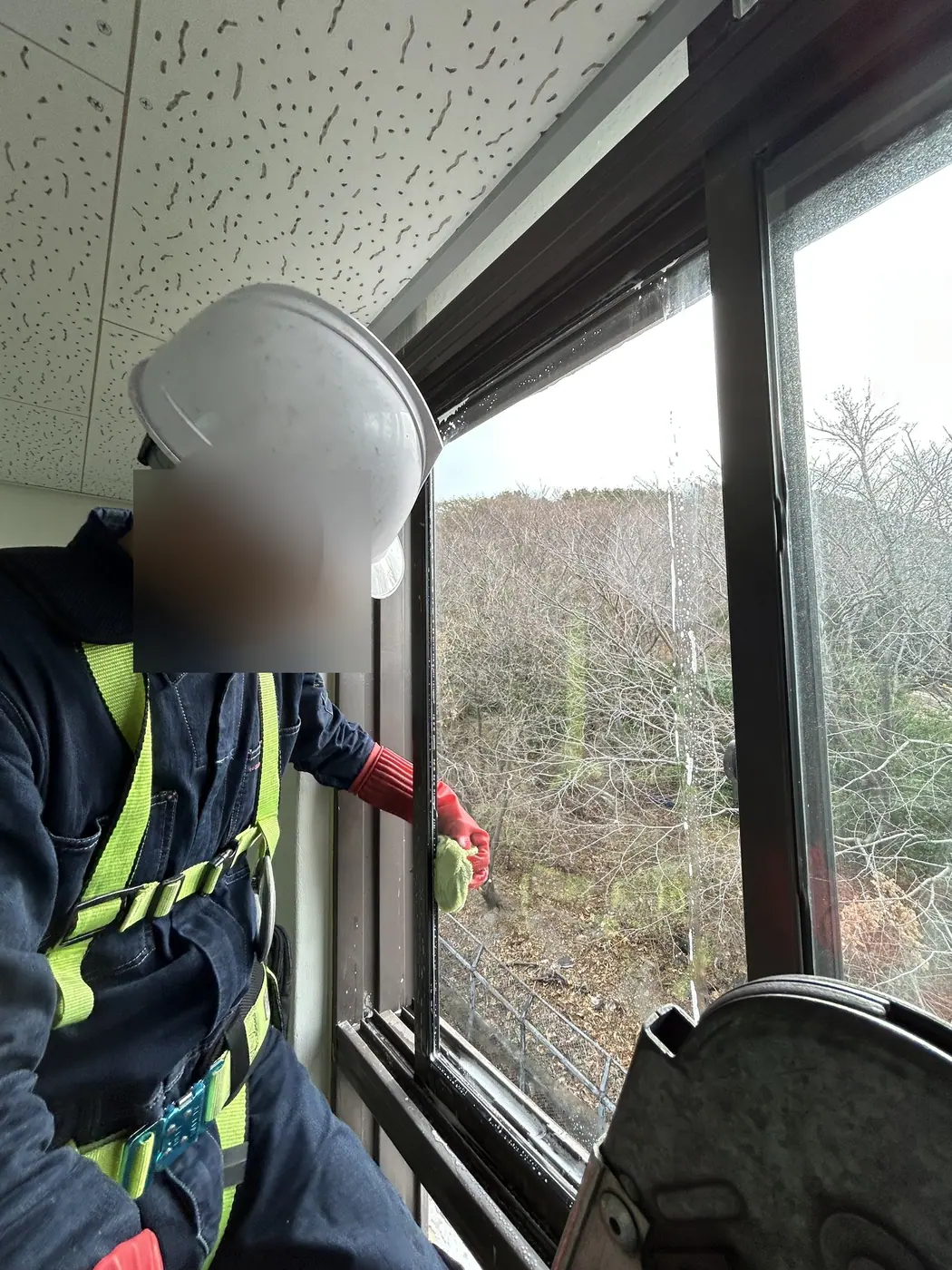 부산 사하구 전시시설에서 안전모와 안전대를 갖춘 작업자가 천장 가까이 달린 창의 틀을 천으로 닦는 모습