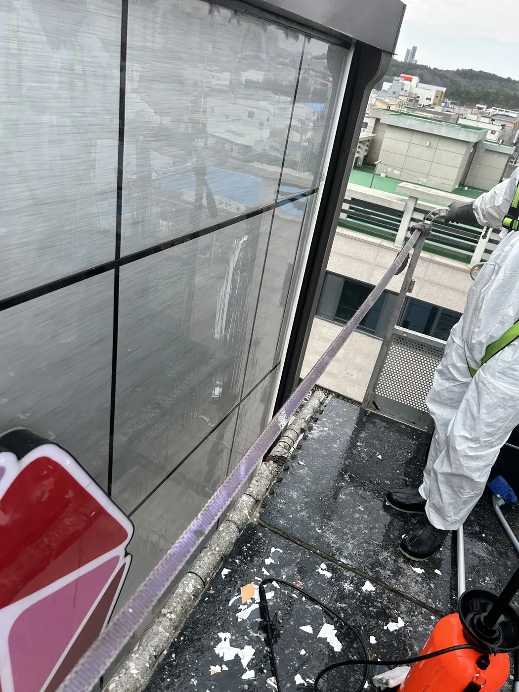 포항 북구 상가건물 옥상 턱에서 보호복을 입은 작업자가 회색 판넬 외벽 윗단에 세척건을 대고 씻는 모습