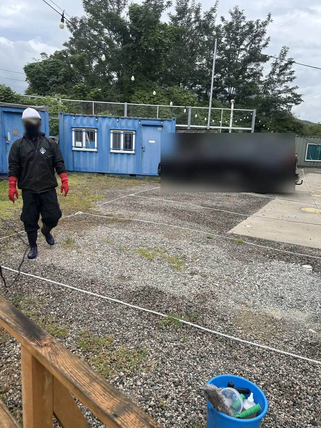 부산 기장 글램핑장 자갈길에서 우비를 입은 작업자가 세척 장비를 메고 텐트 동으로 옮겨 가는 모습