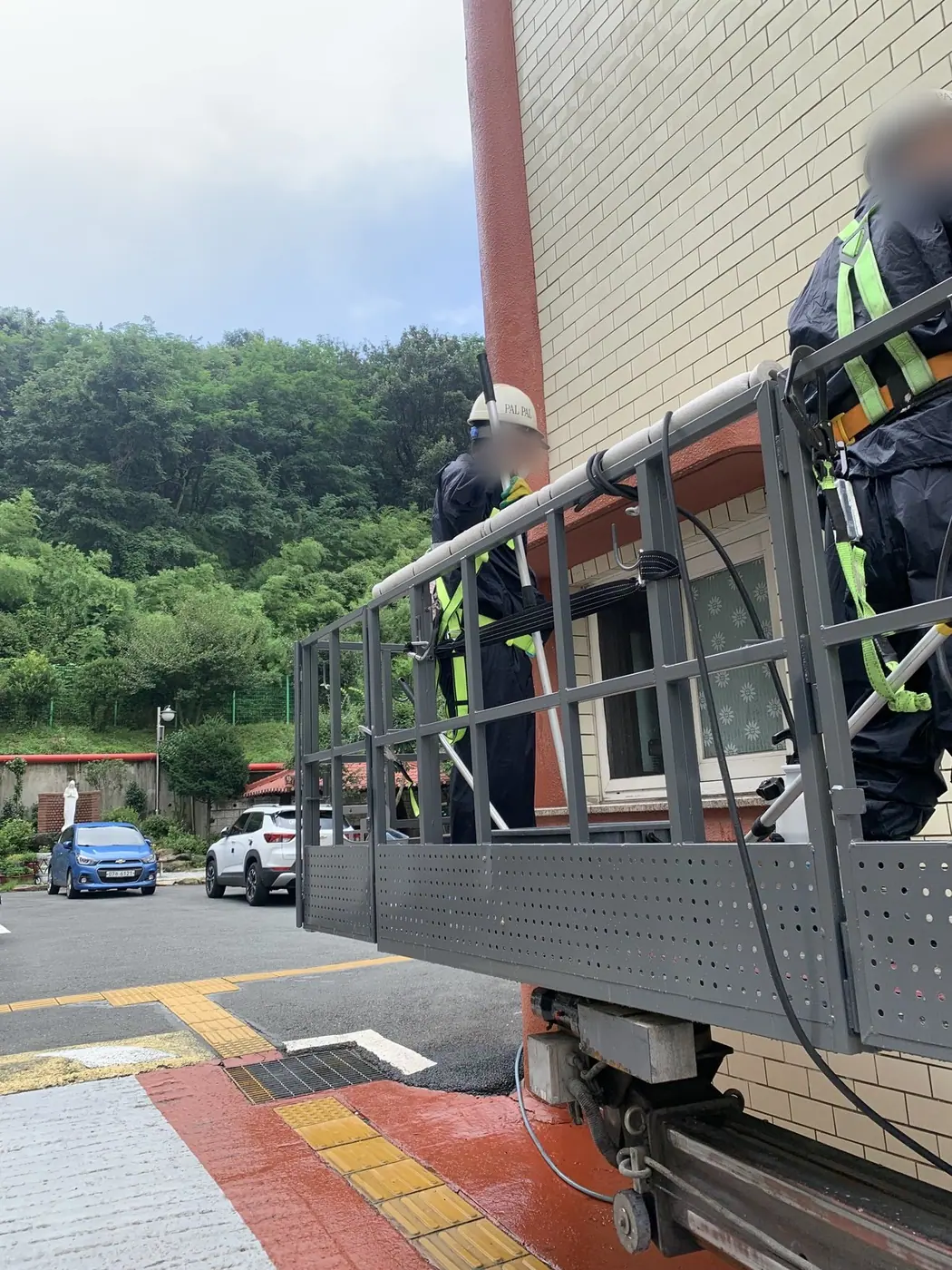 지상에서 두 작업자가 고소작업대 바스켓에 올라 출발을 준비하는 장면
