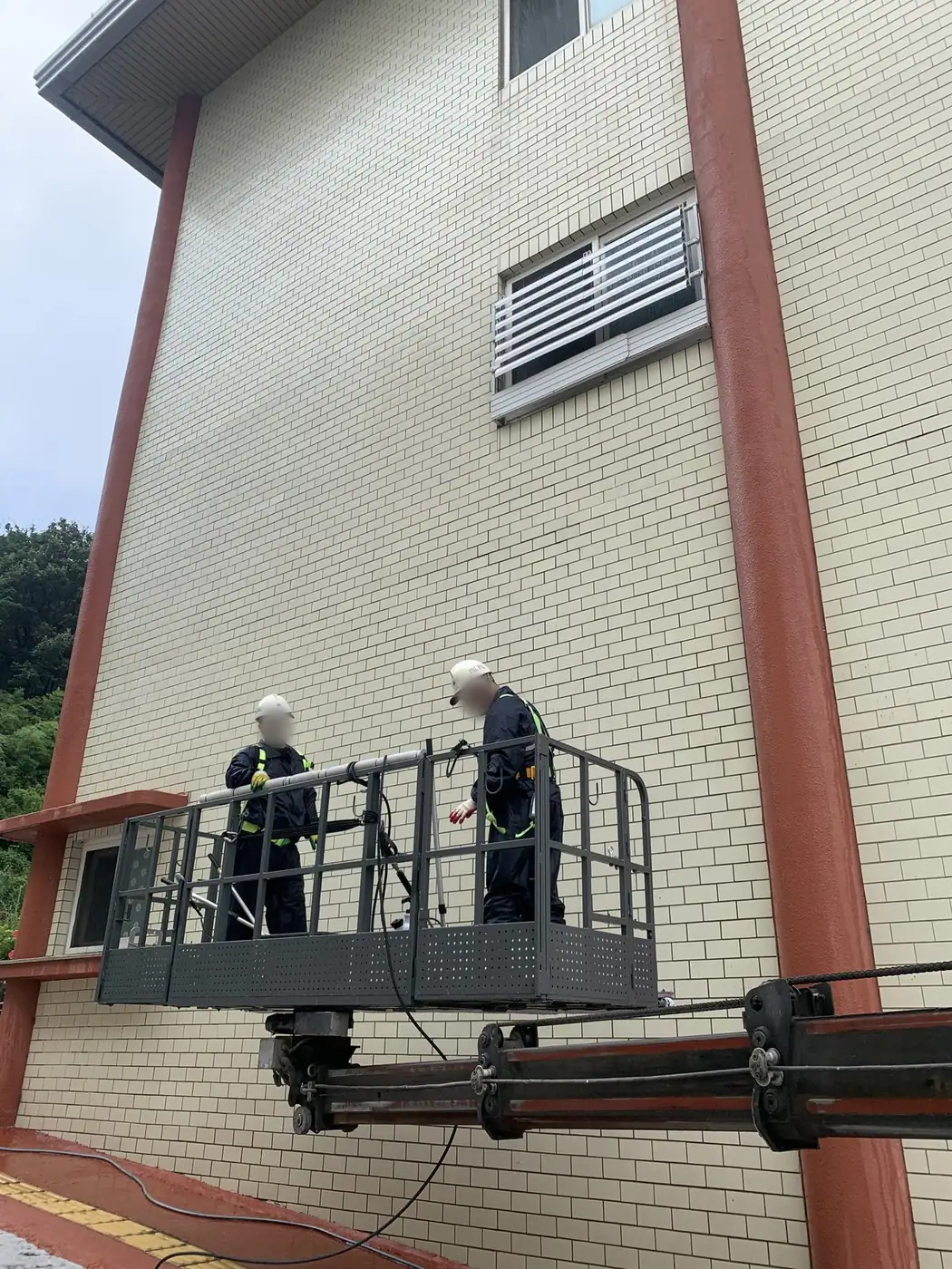 건물 코너 구간에서 두 작업자가 바스켓에 올라 외벽을 세척하는 장면