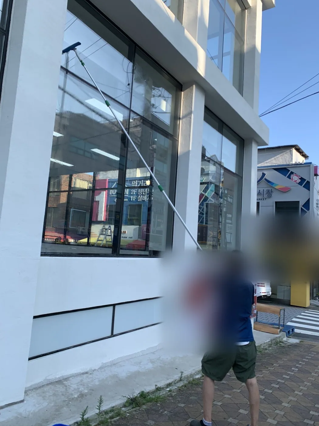 작업자가 상가 전면 유리의 얼룩 구간을 도구로 문질러 닦는 장면