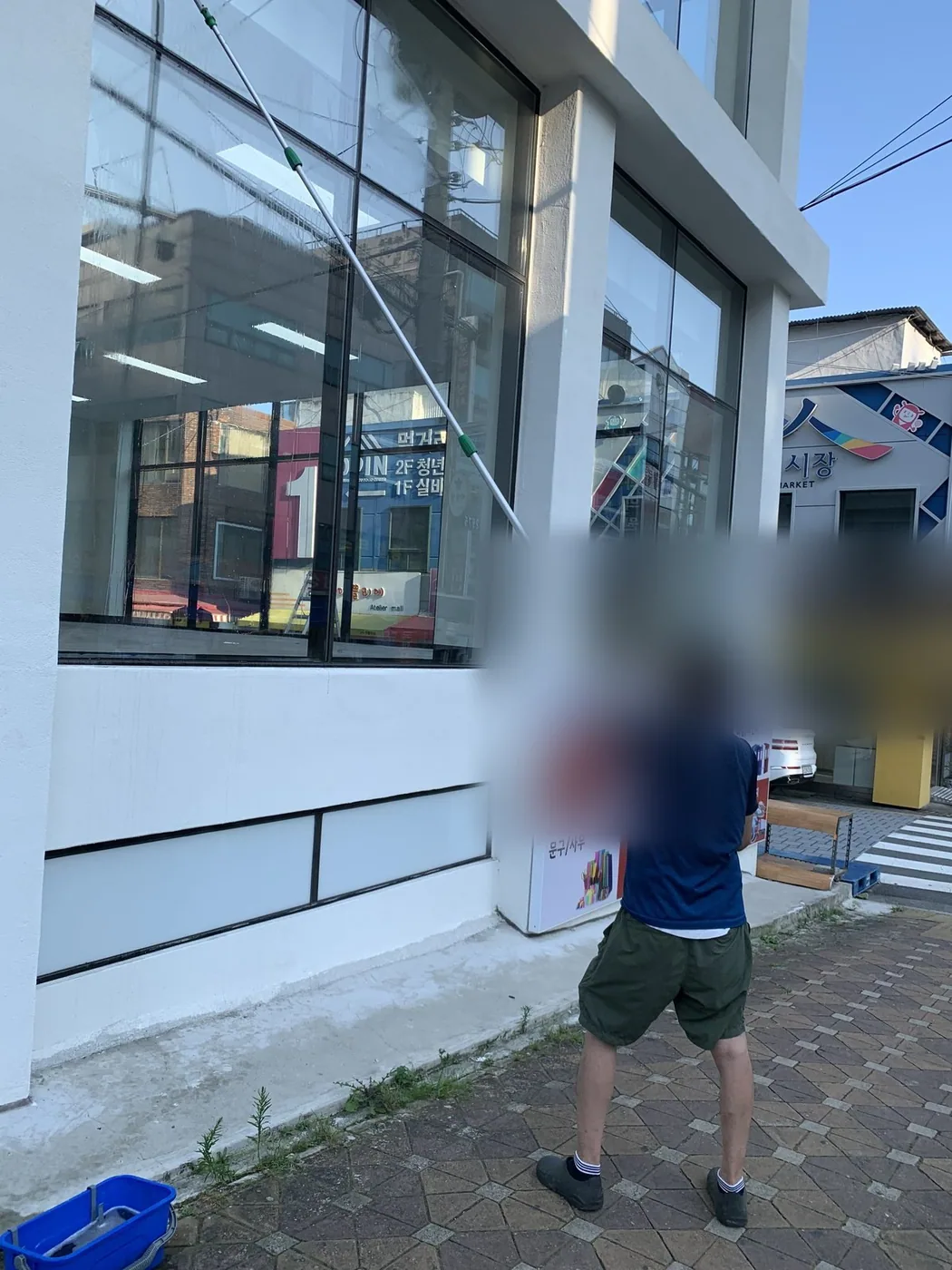 도로변 상가 전면 유리 앞에서 작업자가 도구를 바꿔 가며 작업하는 장면