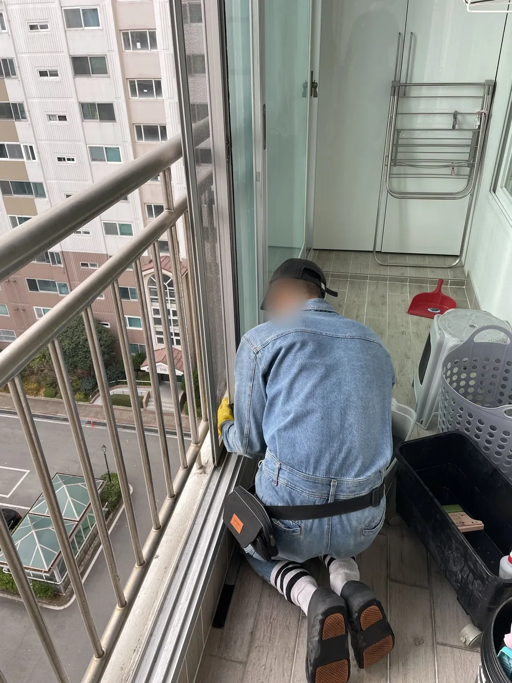 작업자가 베란다 바닥에 자세를 낮추고 창 하부를 세척하는 장면