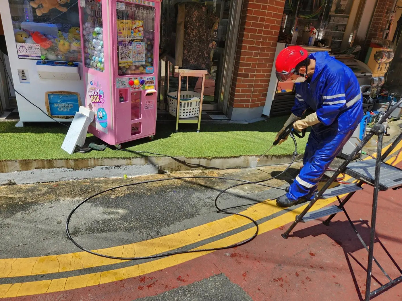 보도 위에 세척기 호스를 벽 쪽으로 정리하고 작업자가 자리를 잡는 장면