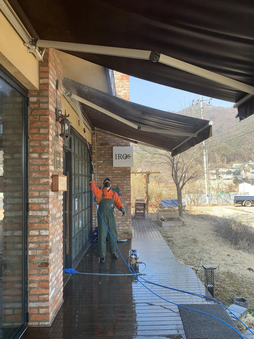 차양 아래 젖은 통로에서 벽돌 벽면 하부를 세척하는 장면