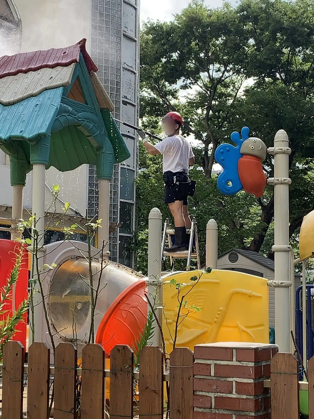 사다리에 올라 놀이터에 접한 건물 벽면을 세척하는 장면