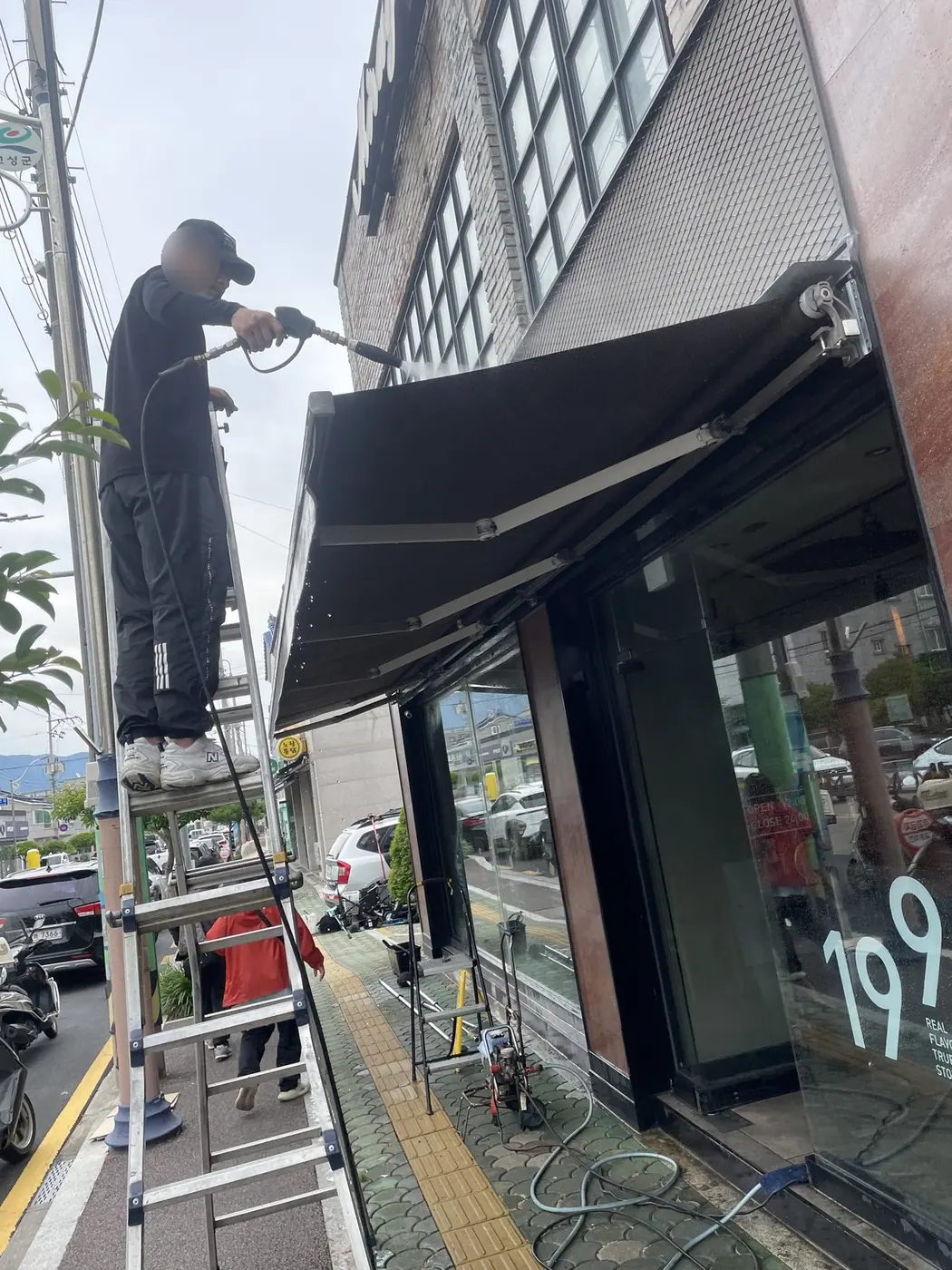 사다리 위 작업자가 금속 판 캐노피 윗면을 각도를 눕혀 세척하는 장면