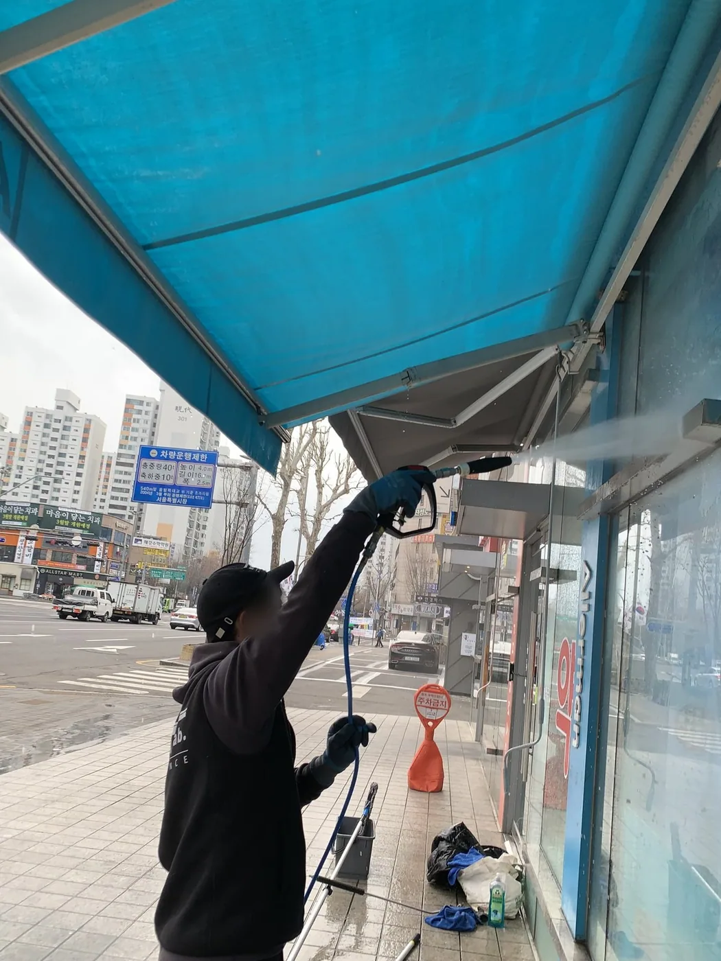 작업자가 어닝 아래에서 위를 향해 물을 분사하며 안쪽 면을 세척하는 장면