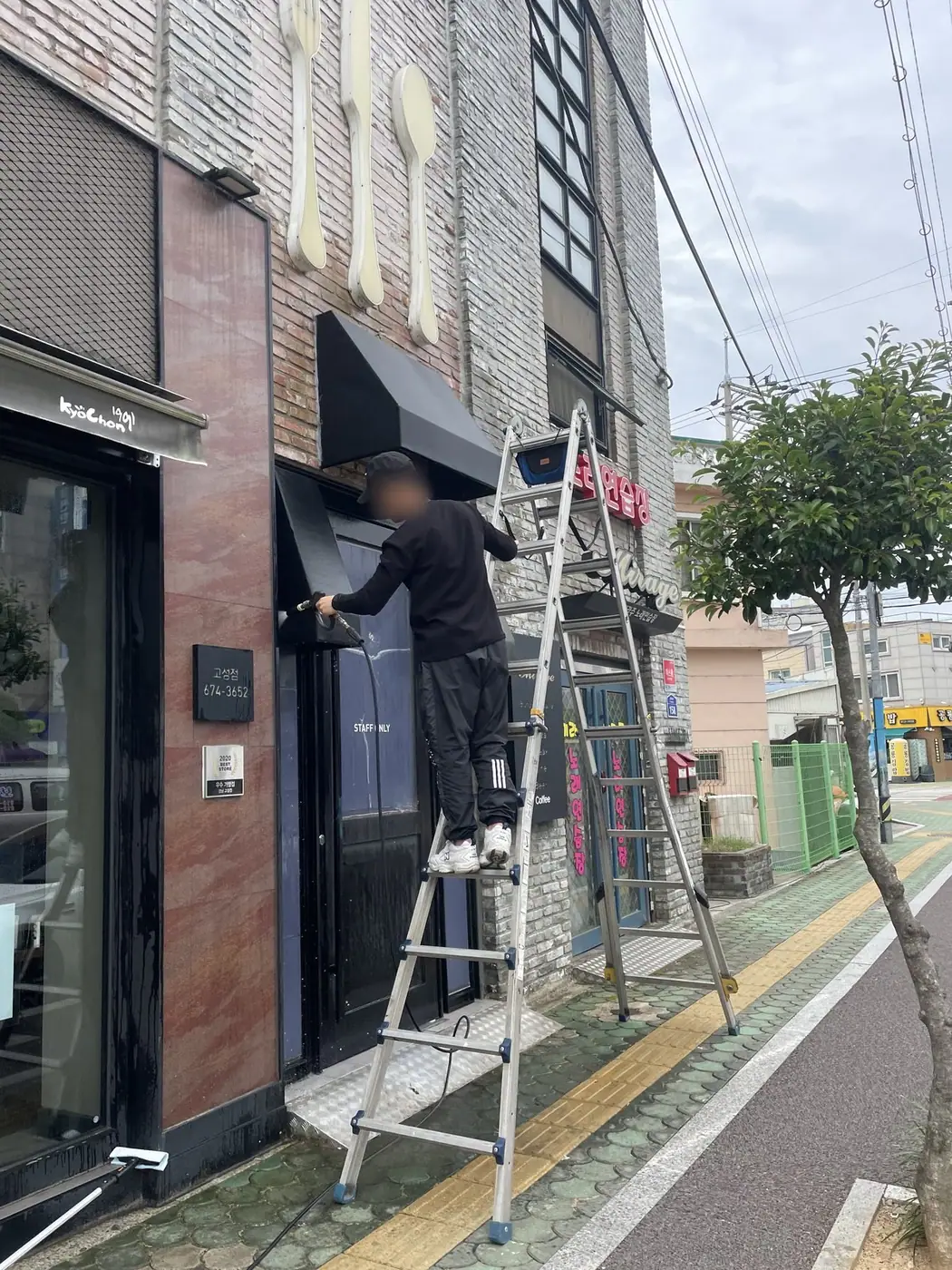 작업을 마친 어닝을 펴 둔 채 출입구 옆 사다리를 정리하는 장면