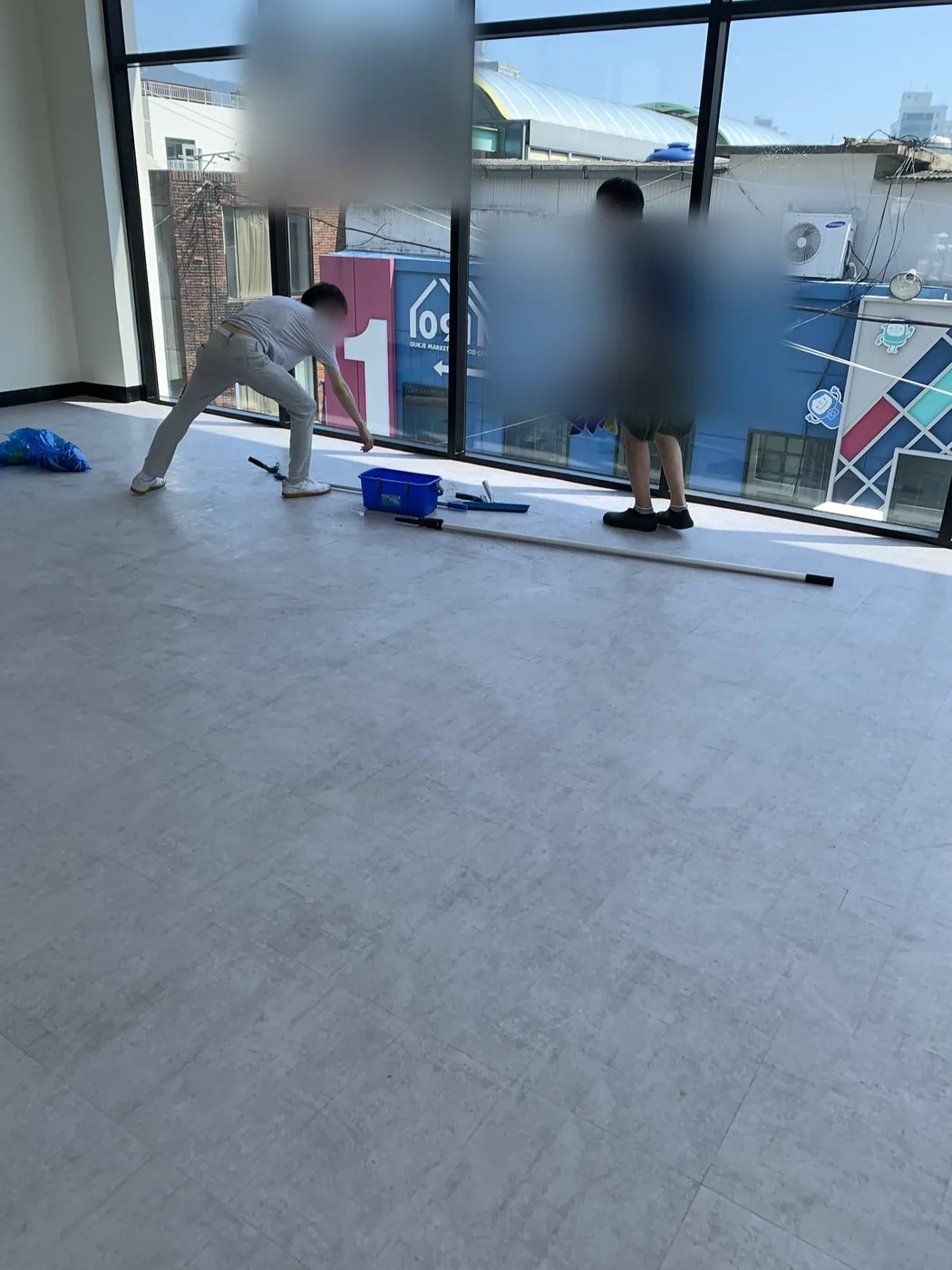 두 작업자가 대형 유리면 앞에서 도구를 나눠 들고 작업하는 장면