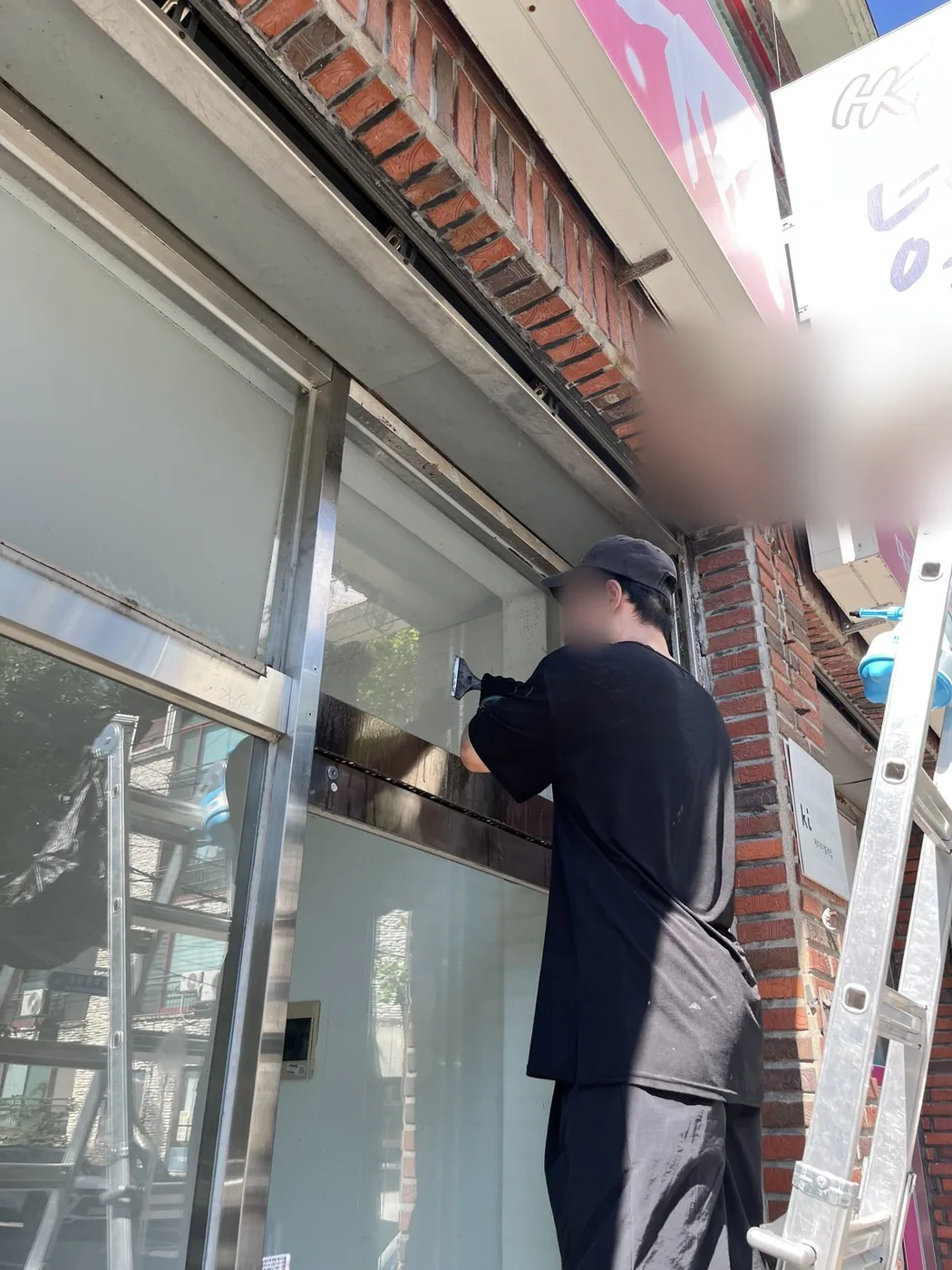 상가 건물 바깥에서 작업자가 미닫이창의 상부 구간을 도구로 세척하는 장면