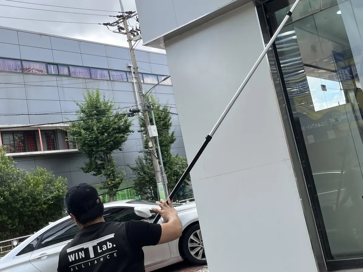 긴 폴대로 매장 모서리 통유리를 닦아 올리는 작업자