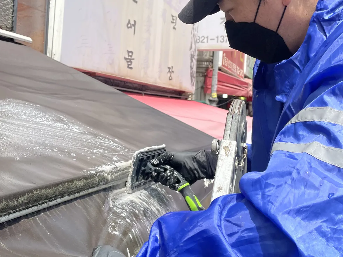 매장 어닝을 고압 건으로 씻어 내는 작업자의 손