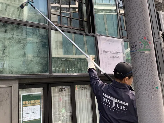 긴 폴대로 건물 외벽 유리를 닦아 올리는 작업자