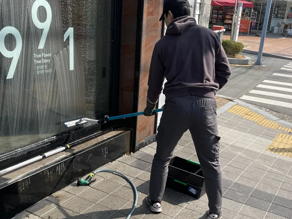 모자를 쓰고 매장 통유리창을 스퀴지로 닦는 작업자